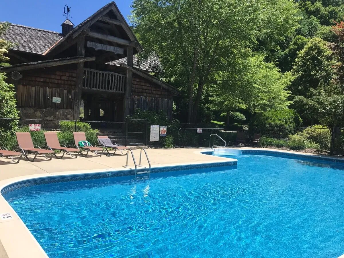 A sparkling swimming pool nestled amidst lush greenery, with inviting lounge chairs and a charming wooden cabin in the background. The setting is relaxed, with the pool ready for family fun and outdoor recreation.