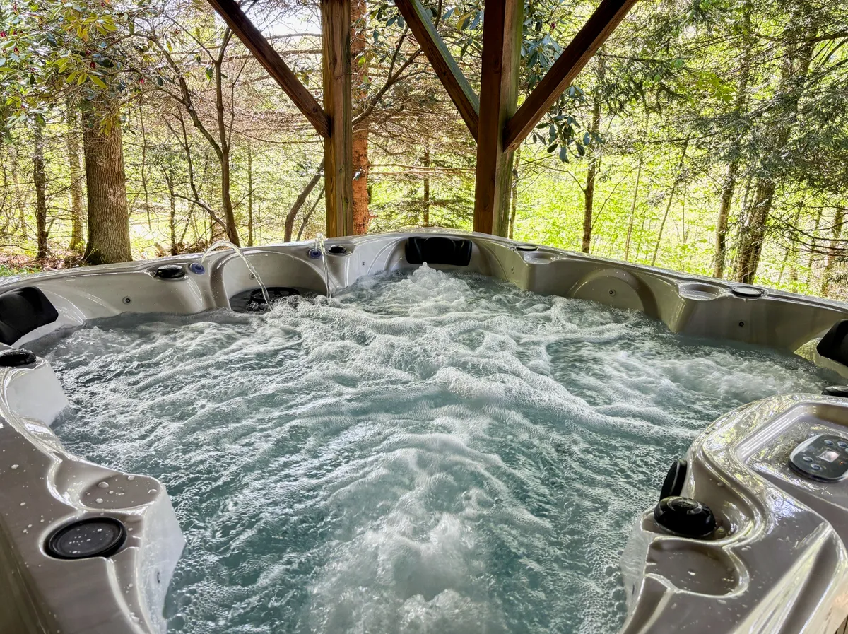 A brand-new hot tub is nestled on a wooden deck, surrounded by towering trees. The bubbling water and open sky invite relaxation, and the tranquil forest setting offers privacy and a sense of immersion in nature. The deck area appears spacious, ideal for stargazing or enjoying the fresh mountain air.