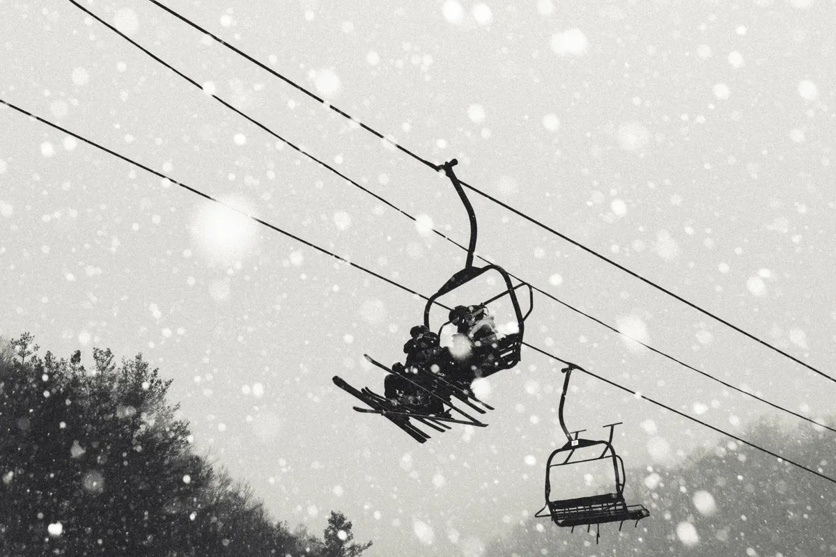 A ski lift glides above snow-covered trees as gentle snowflakes fall, capturing the thrill and tranquility of winter at Hatley Pointe. The wintry landscape sets the scene for skiing and snowboarding adventures.