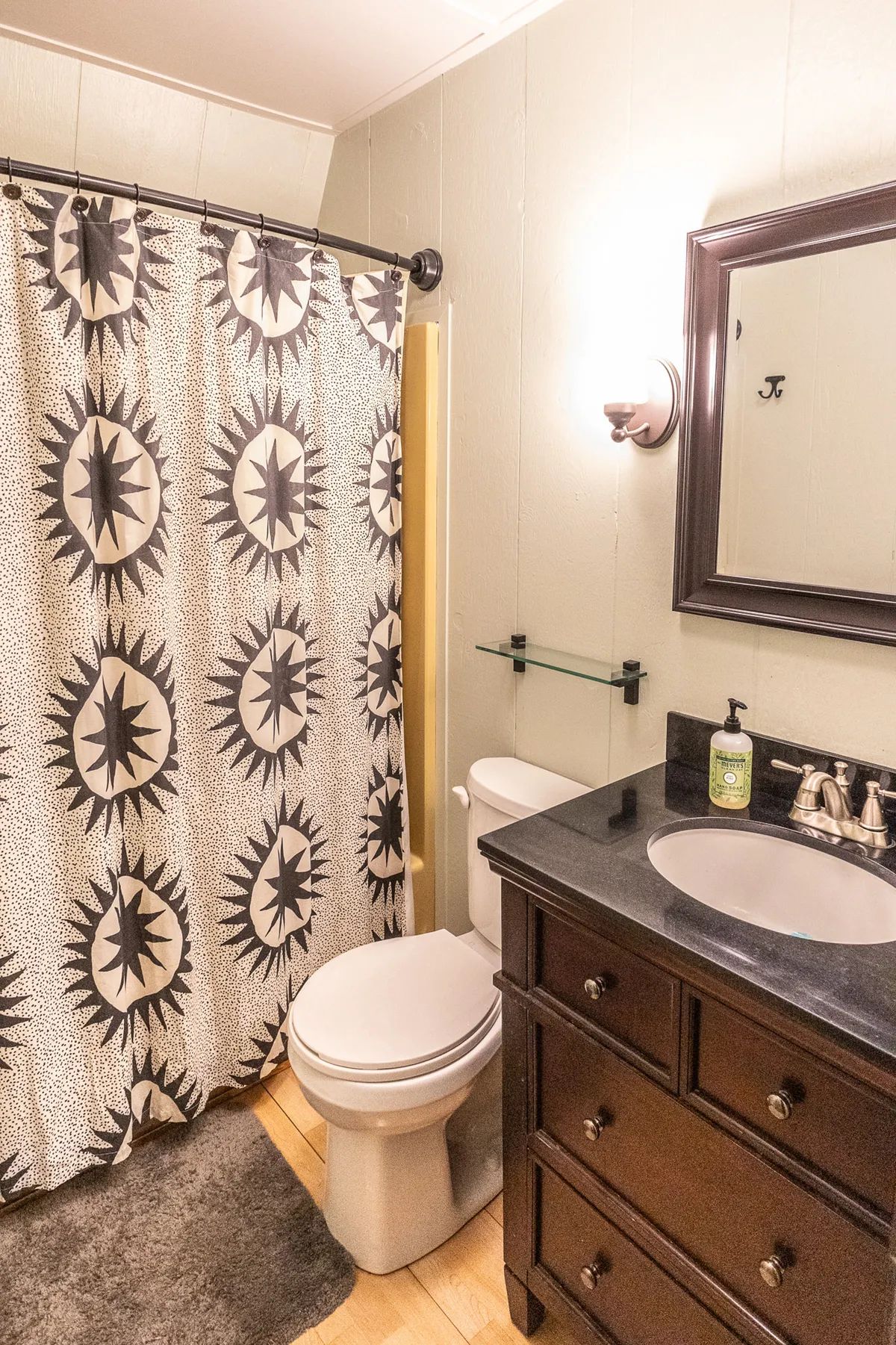 A modern bathroom with a dark wood vanity, sleek sink, and a whimsical shower curtain with a star pattern. The soft lighting and clean surfaces create a soothing, spa-like setting for self-care routines.