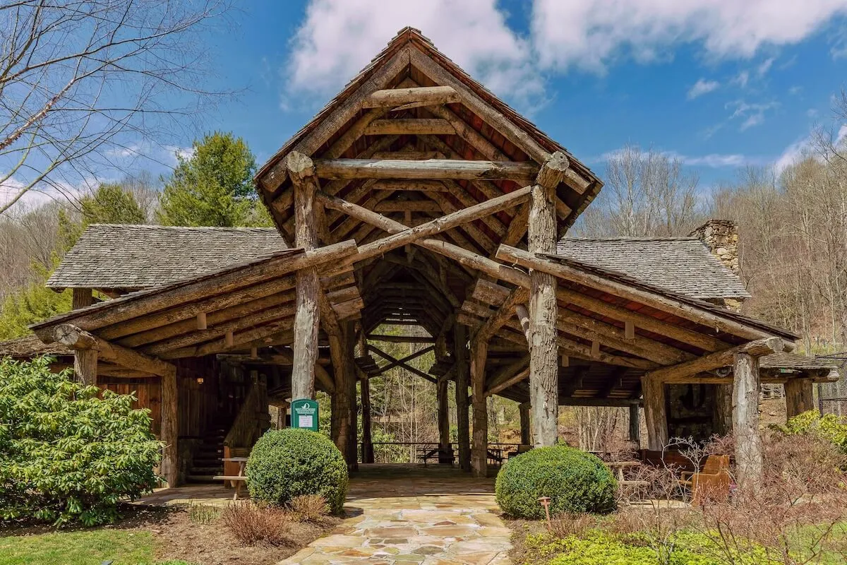 A welcoming log structure with a stone pathway and landscaped shrubs, ideal for gatherings and family reunions. The surroundings are lush and green, suggesting opportunities for nature walks and outdoor exploration starting right from the cabin.